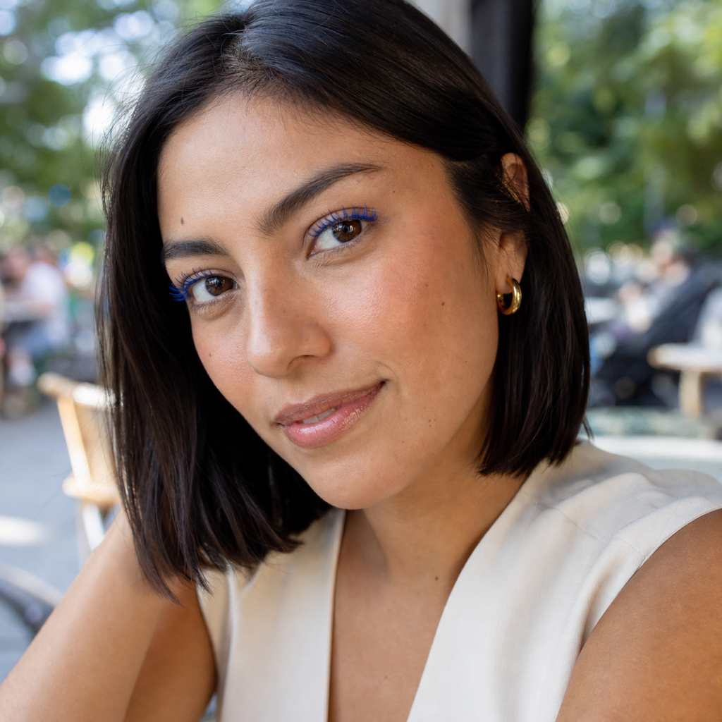 Natural makeup with vivid cobalt blue mascara, peach blush, glossy lip and an ivory blouse